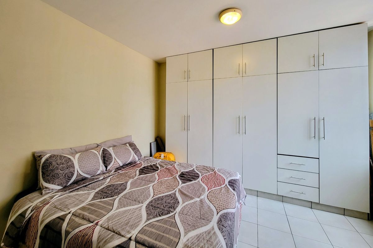 A well-maintained bedroom featuring extensive white built-in cupboards, neutral wall finishes, and clean tiled flooring.