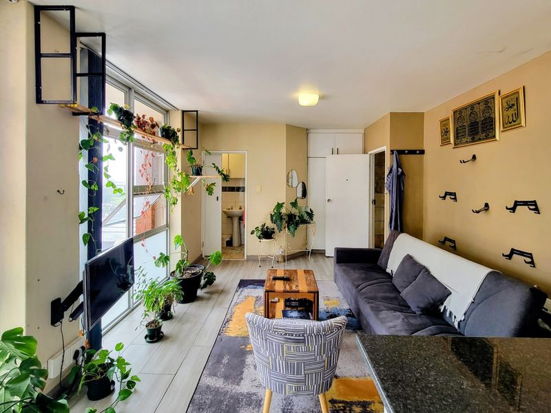 Open plan living area featuring large windows, tiled flooring, and built-in storage cupboards, offering a functional space with potential for modern updates.