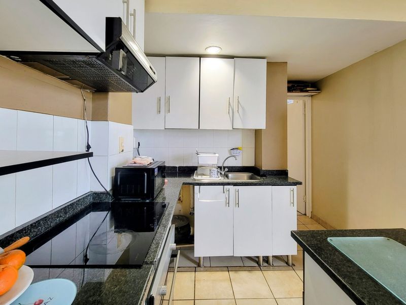 Compact kitchen featuring granite countertops, white cabinetry, an electric hob with extractor fan, and tiled flooring.