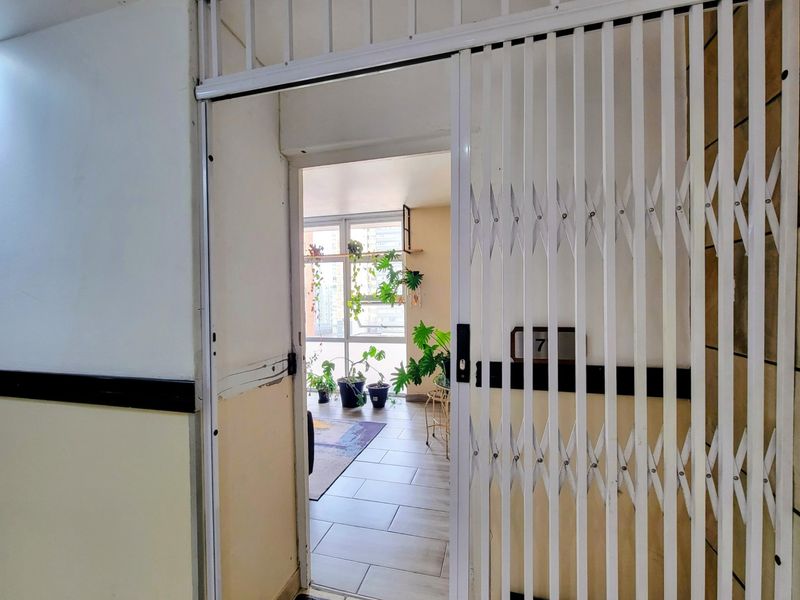 Entrance area featuring a white security gate, tiled flooring, and a view through to a bright living space with large windows.