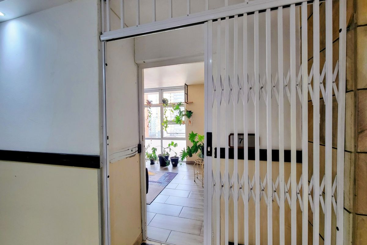 Entrance area featuring a white security gate, tiled flooring, and a view through to a bright living space with large windows.