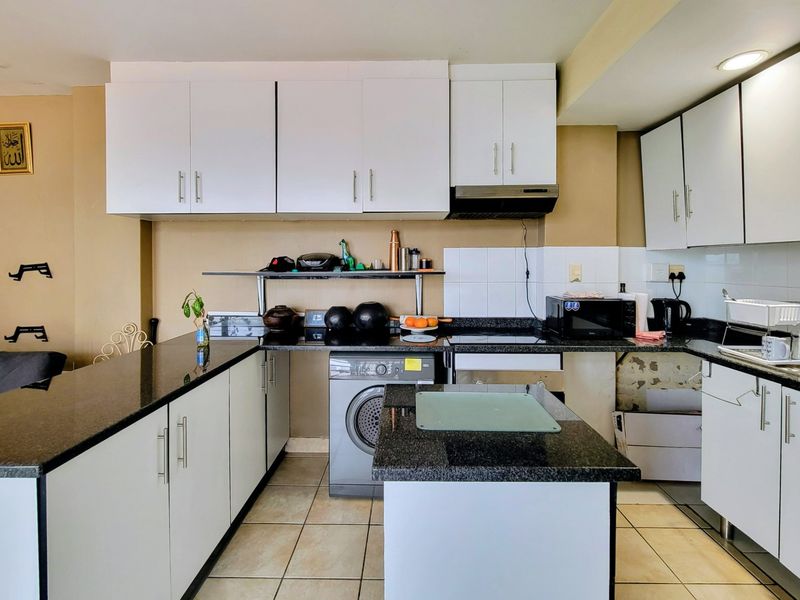 A functional kitchen featuring white cabinetry, granite countertops, a tiled backsplash, and integrated laundry facilities, offering a practical layout for daily use.