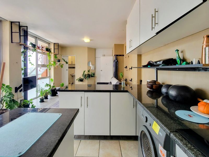 Open-plan kitchen and living area featuring granite countertops, modern cabinetry, integrated laundry appliance, and expansive floor-to-ceiling windows providing natural light.