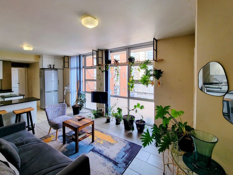 An open-plan living and kitchen area featuring large windows, tiled flooring, and built-in kitchen cabinetry with granite countertops.