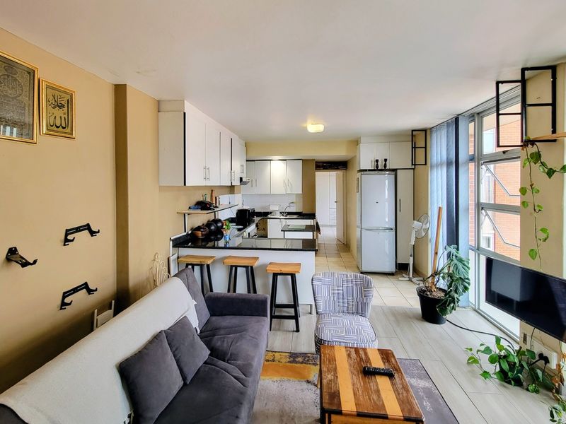 Open-plan living and kitchen area featuring modern white cabinetry, granite countertops, a breakfast bar, and large windows providing ample natural light.