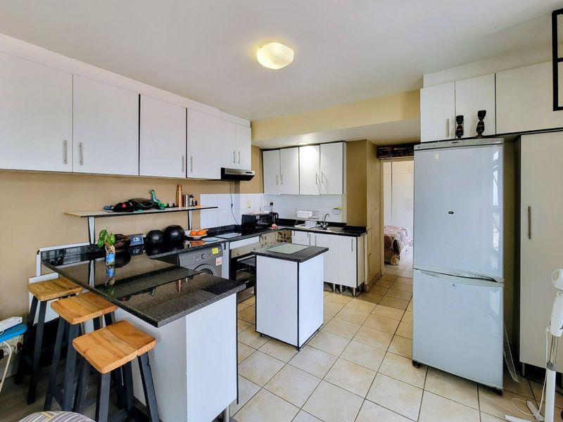 A functional kitchen featuring white cabinetry, dark granite countertops, tiled flooring, and an integrated extractor fan, offering a practical layout for daily use.