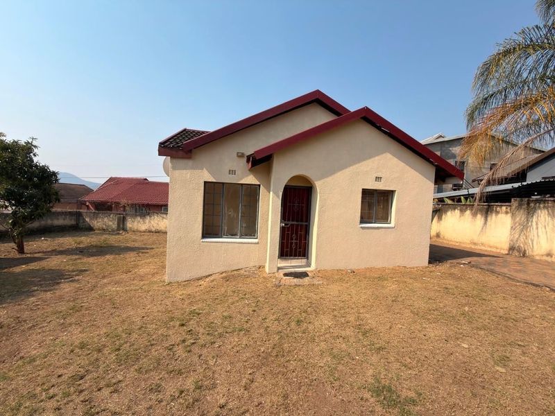 Front view of a detached single-story house featuring a tiled roof, security gate, and surrounding perimeter wall on a dry grass plot.