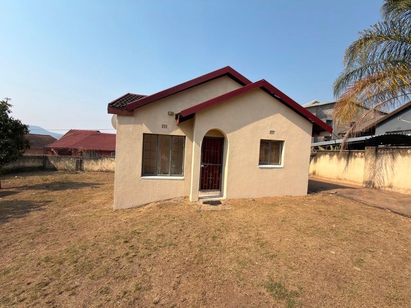 A detached single-story house featuring a tiled roof, plastered exterior, and a secure entrance gate, set within a fenced residential plot.