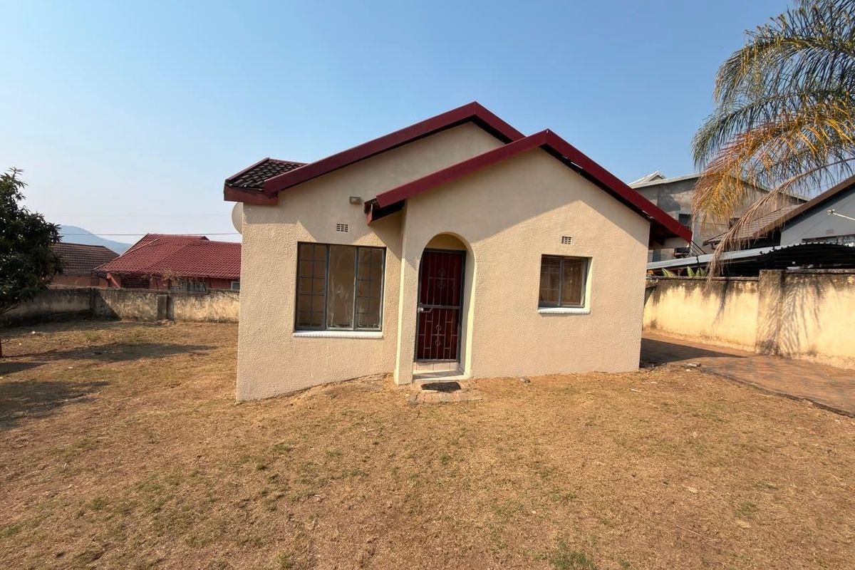 A detached single-story house featuring a tiled roof, plastered exterior, and a secure entrance gate, set within a fenced residential plot.
