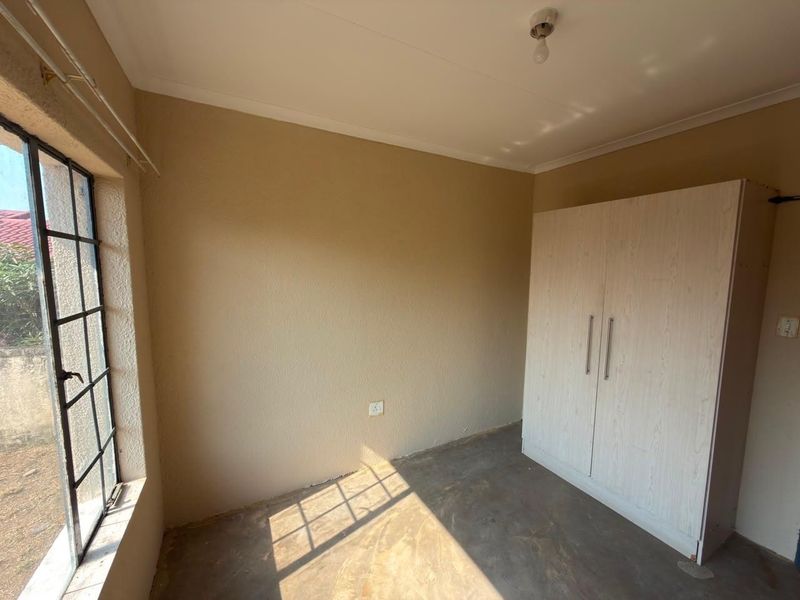 A simple bedroom featuring a built-in wardrobe, steel-framed window, and neutral wall finishes, ready for flooring and lighting upgrades.