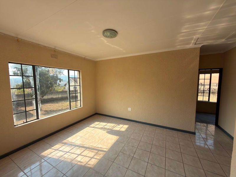 A bright, empty living room featuring neutral textured walls, tiled flooring, and a large window providing natural light.