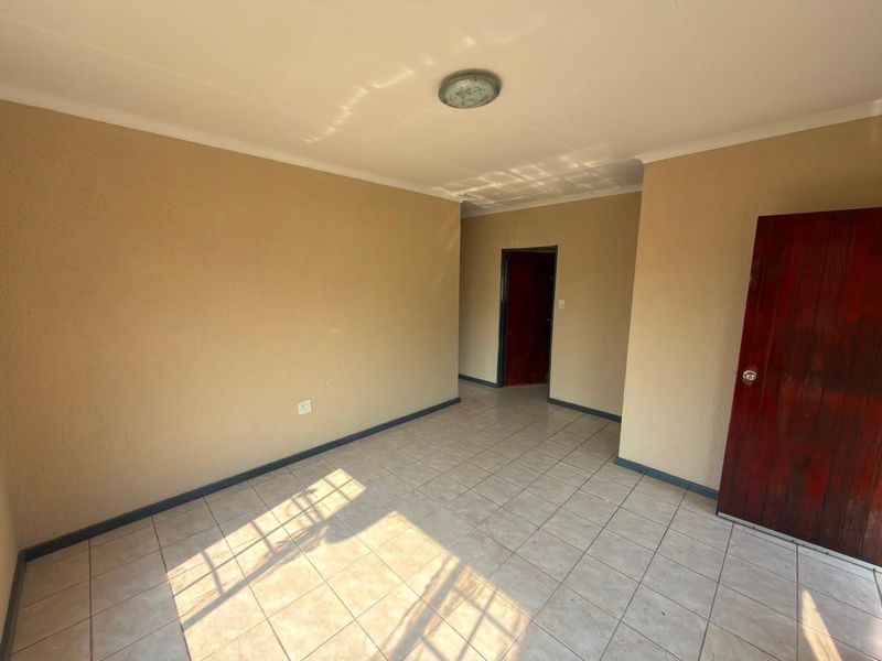 An empty living area featuring neutral walls, tiled flooring, and a timber door, providing a blank canvas for interior design.