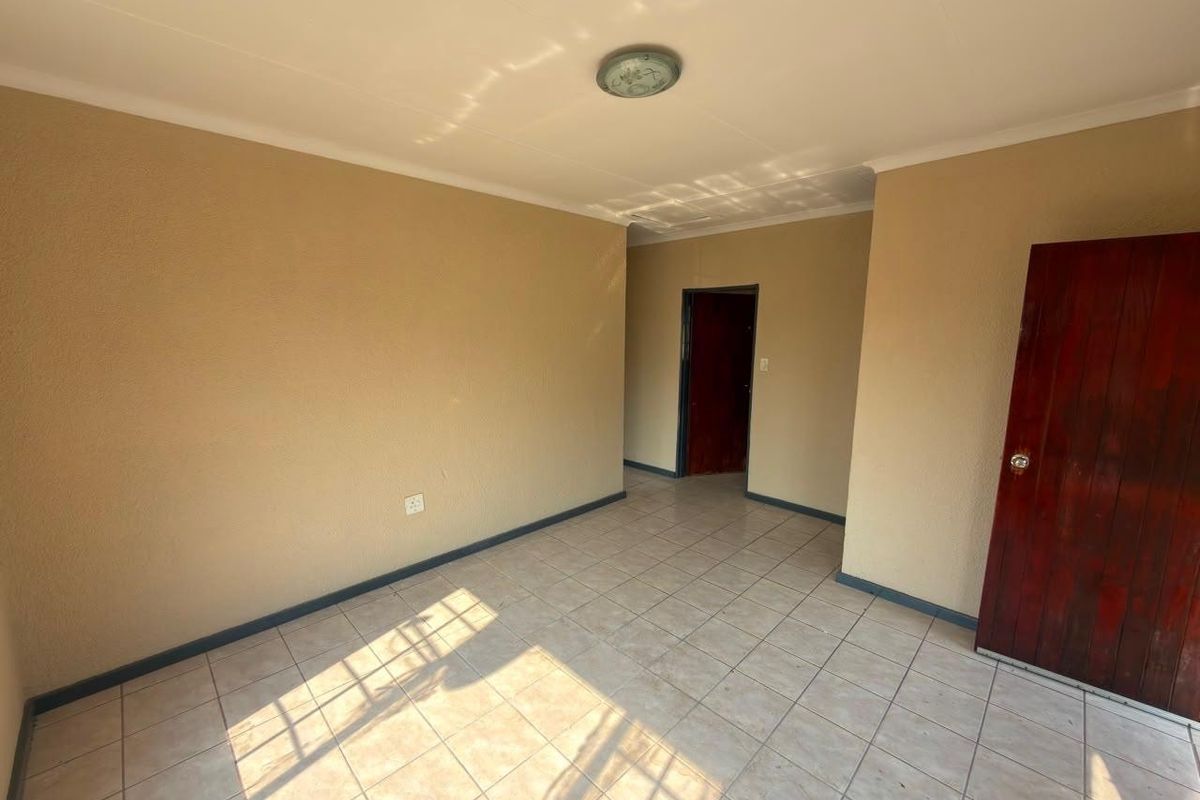 An empty living area featuring neutral walls, tiled flooring, and a timber door, providing a blank canvas for interior design.