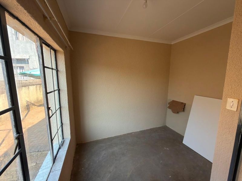 An empty bedroom featuring a steel-framed window, textured walls, and an unfinished concrete floor, offering a blank canvas for renovation.