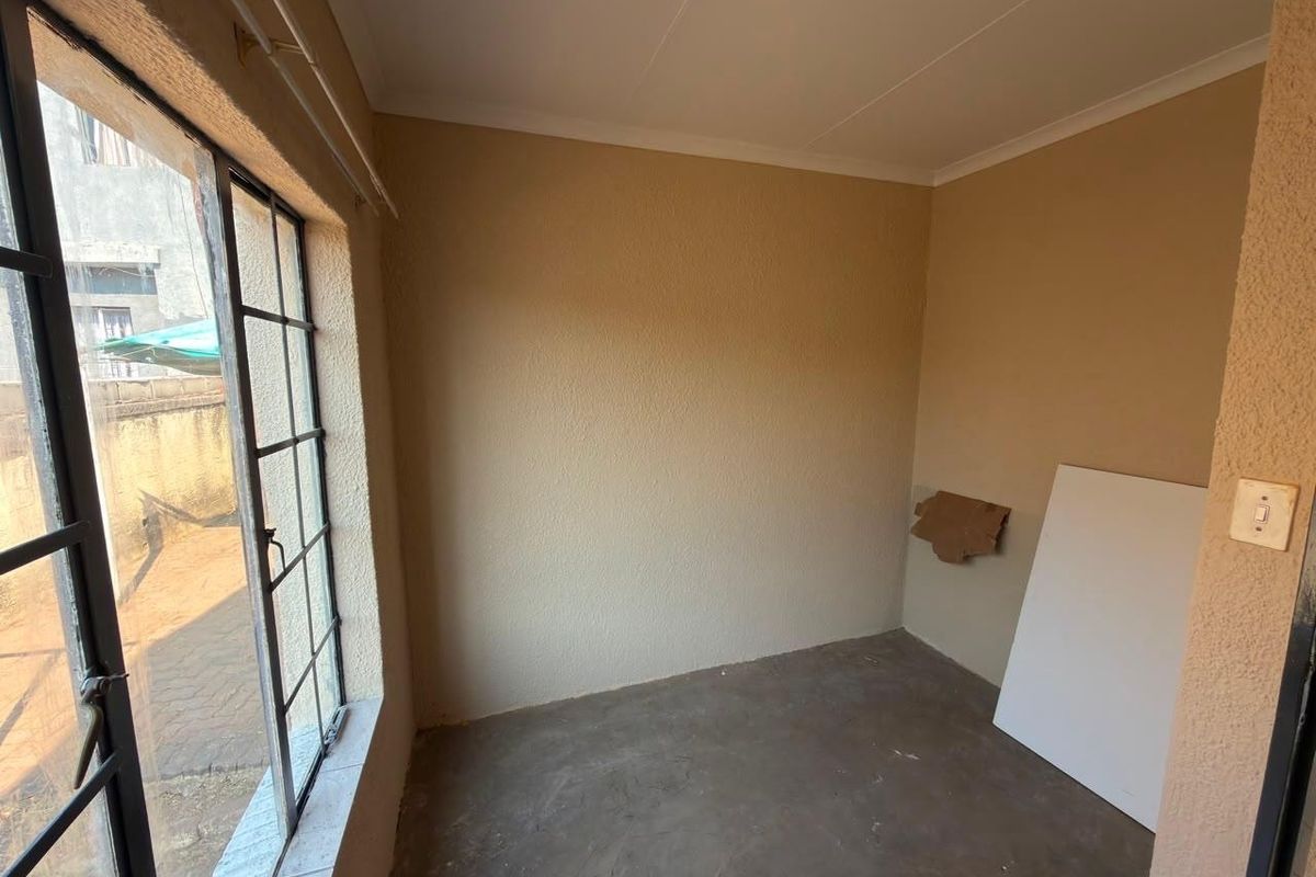 An empty bedroom featuring a steel-framed window, textured walls, and an unfinished concrete floor, offering a blank canvas for renovation.