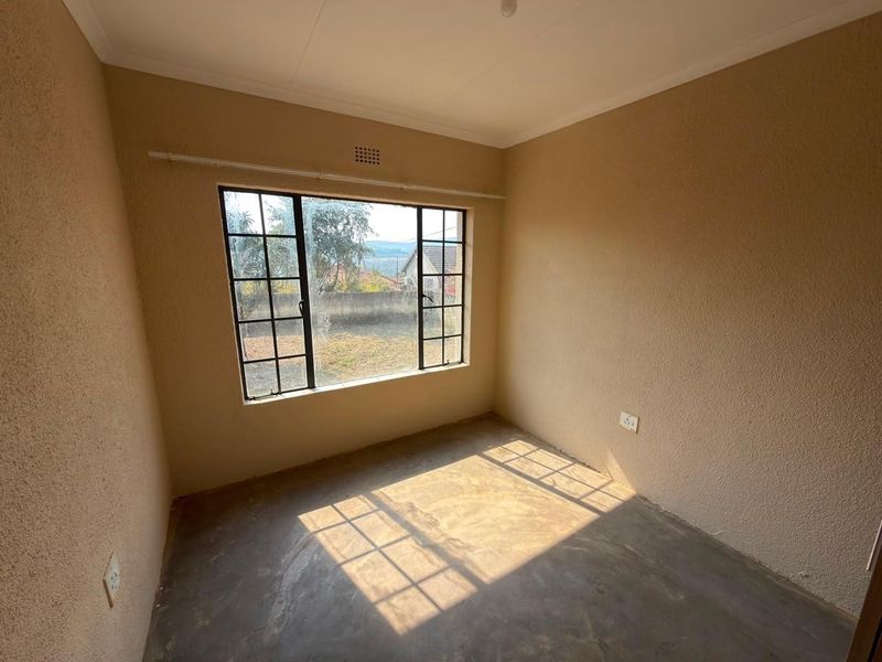 An empty bedroom featuring textured walls, a steel-framed window, and concrete flooring, offering a blank canvas for renovation or interior design.