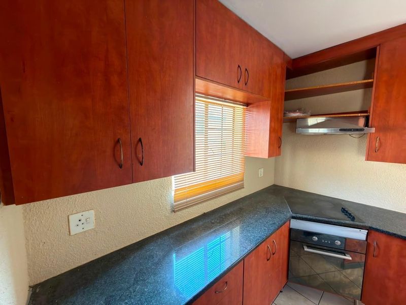 A functional kitchen featuring warm-toned built-in cabinetry, dark granite countertops, and integrated cooking appliances including an oven, hob, and extractor fan.