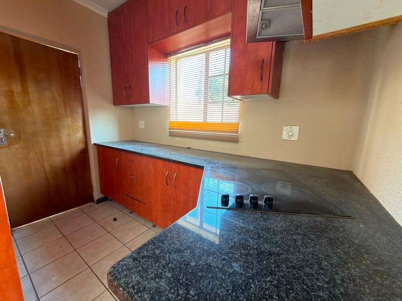 A functional kitchen featuring dark laminate countertops, built-in wooden cabinetry, an electric hob with extractor fan, and tiled flooring.