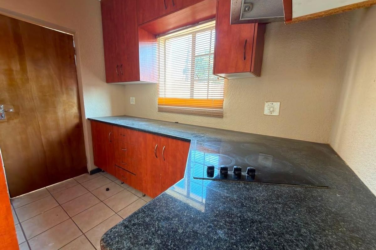 A functional kitchen featuring dark laminate countertops, built-in wooden cabinetry, an electric hob with extractor fan, and tiled flooring.