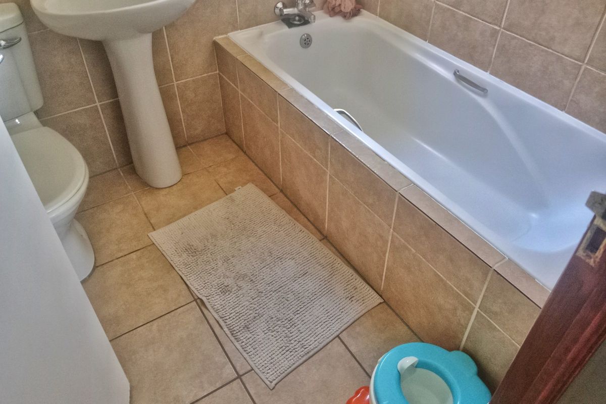 A functional bathroom featuring a pedestal washbasin, toilet, and bathtub with neutral wall and floor tiling.