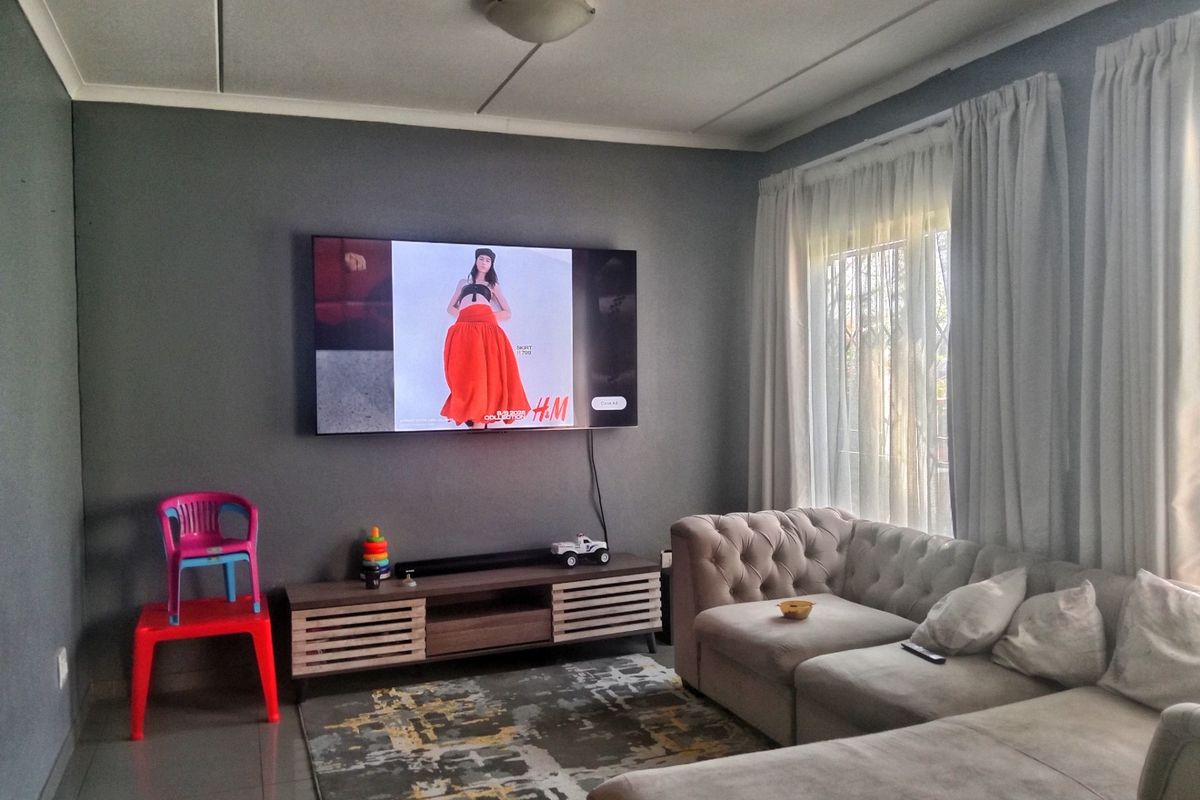 A comfortable living room featuring tiled flooring, neutral wall tones, and large windows with curtain tracks, providing a functional and inviting space.