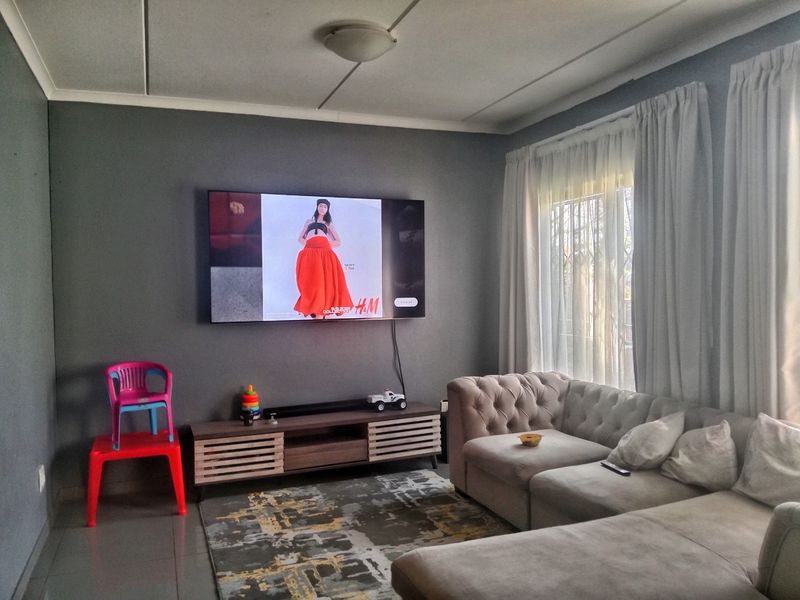 A comfortable living room featuring tiled flooring, neutral wall tones, and large windows with curtain tracks, providing a functional and inviting space.