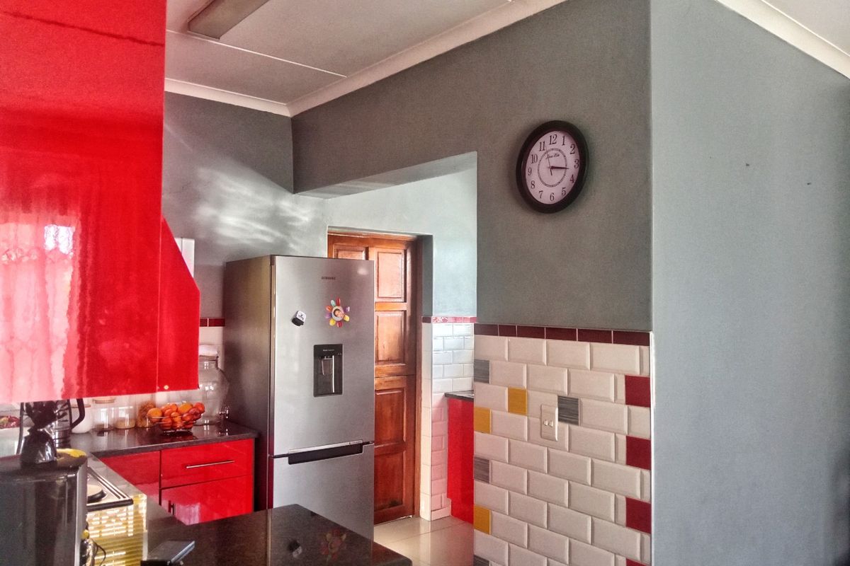 A kitchen featuring red cabinetry, granite countertops, and a decorative subway tile backsplash with accent colors.