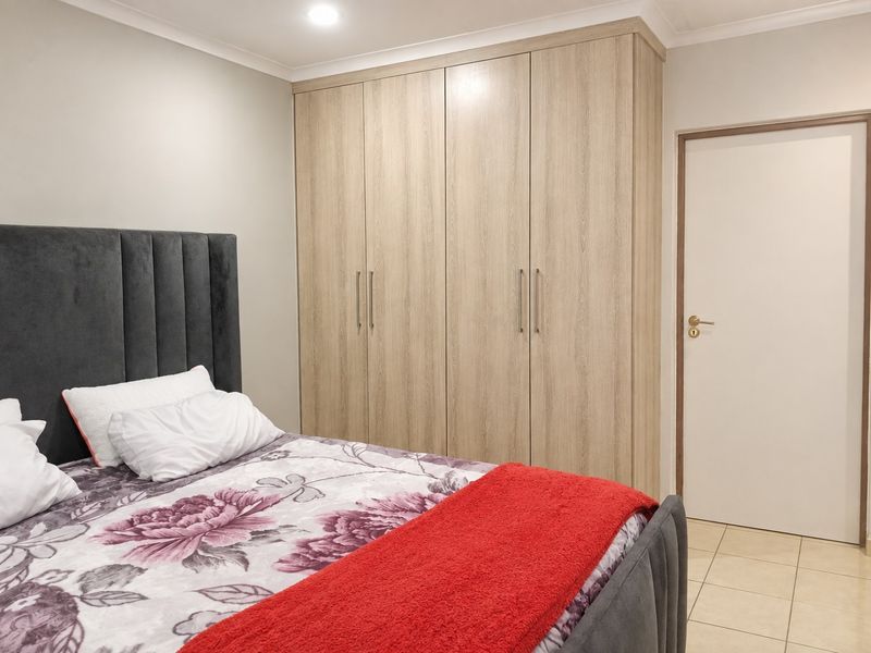 A well-maintained bedroom featuring light wood-grain built-in wardrobes, recessed ceiling lighting, and neutral tiled flooring.