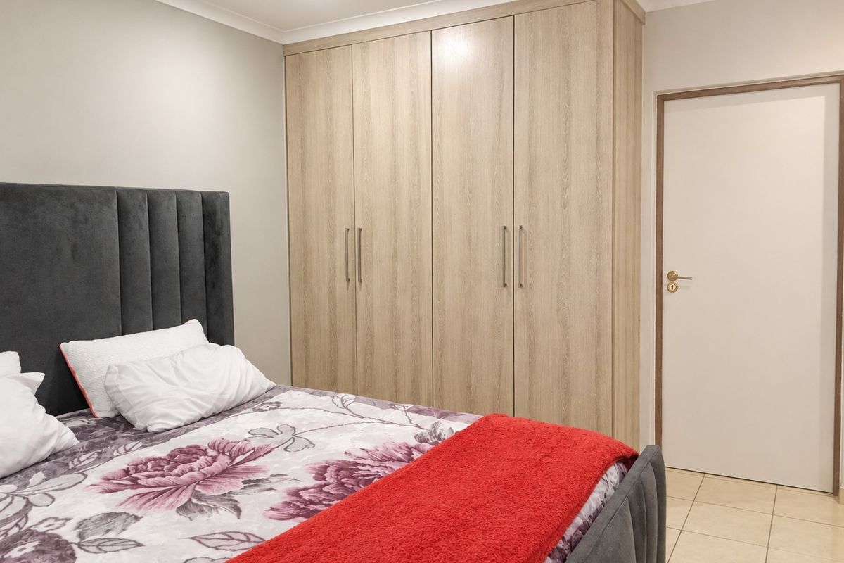 A well-maintained bedroom featuring light wood-grain built-in wardrobes, recessed ceiling lighting, and neutral tiled flooring.