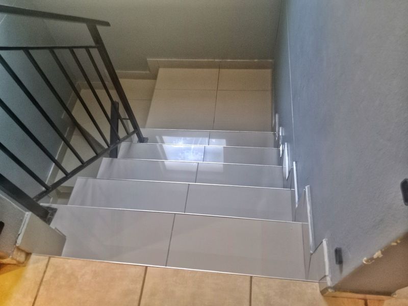 A staircase featuring tiled steps and a black metal balustrade, showing signs of unfinished wall finishes and base detailing.