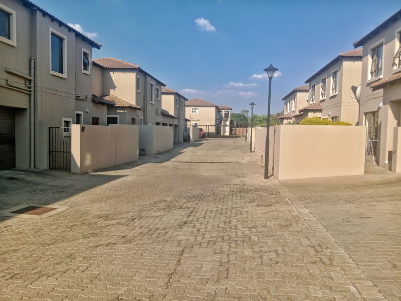A view of the paved residential complex driveway flanked by multi-story townhouse units with boundary walls and street lighting.