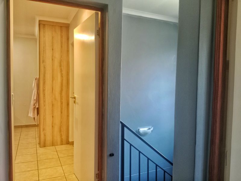 A view from a hallway showing a tiled transition area with built-in cabinetry and a staircase with a metal balustrade.