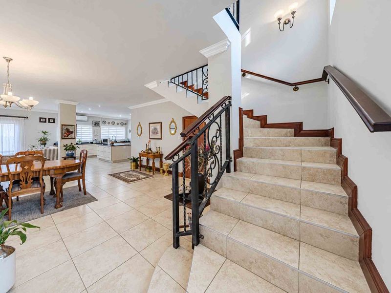 Spacious open-plan living area featuring a tiled staircase with wrought iron railings, flowing into a modern kitchen and dining space.