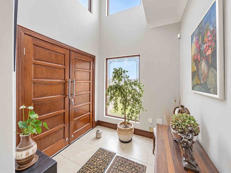 Spacious double-volume entrance hall featuring a grand timber double door, tiled flooring, and abundant natural light from high-level clerestory windows.