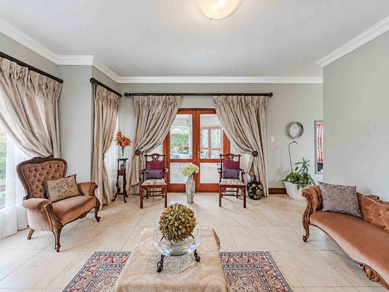 A well-maintained living room featuring neutral tiled flooring, crown molding, and double wooden doors leading to an outdoor patio area.