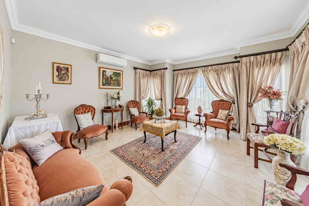 A spacious living room featuring neutral tiled flooring, cove cornicing, and a wall-mounted split-system air conditioner, offering a comfortable and well-maintained living space.