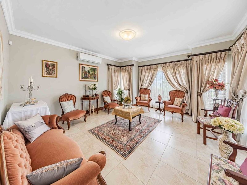 A spacious living room featuring neutral tiled flooring, cove cornicing, and a wall-mounted split-system air conditioner, offering a comfortable and well-maintained living space.