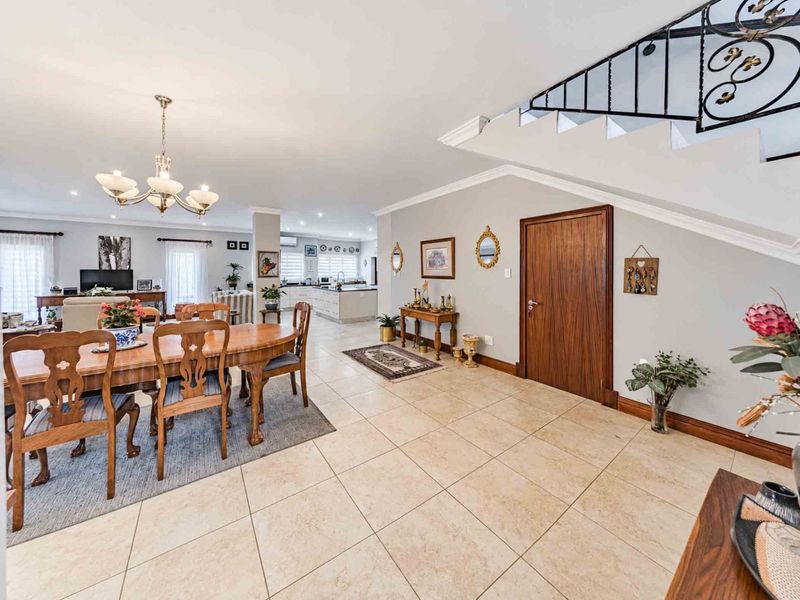 Spacious open-plan living and dining area featuring tiled flooring, crown molding, and a decorative wrought iron staircase railing leading to the upper level.