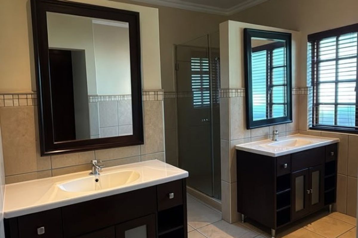 Spacious bathroom featuring a double vanity with dark cabinetry, tiled flooring, and a separate glass-enclosed shower area.