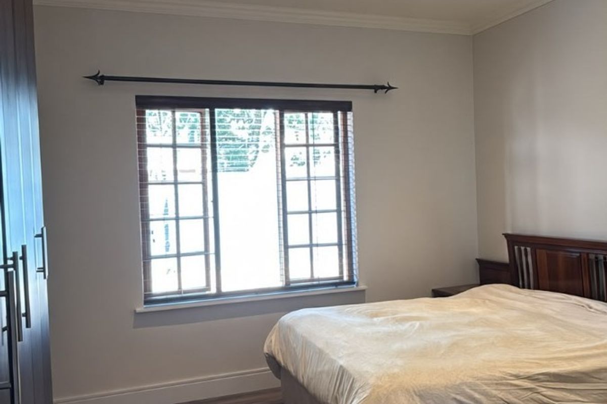 A well-maintained bedroom featuring laminate flooring, built-in cupboards, recessed downlighting, and a window with fitted wooden blinds.