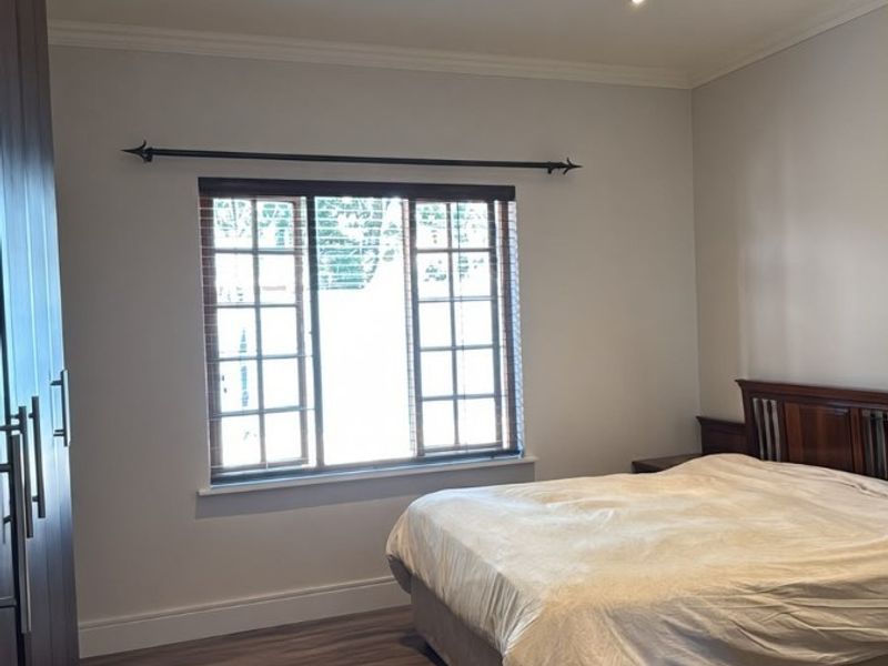 A well-maintained bedroom featuring laminate flooring, built-in cupboards, recessed downlighting, and a window with fitted wooden blinds.