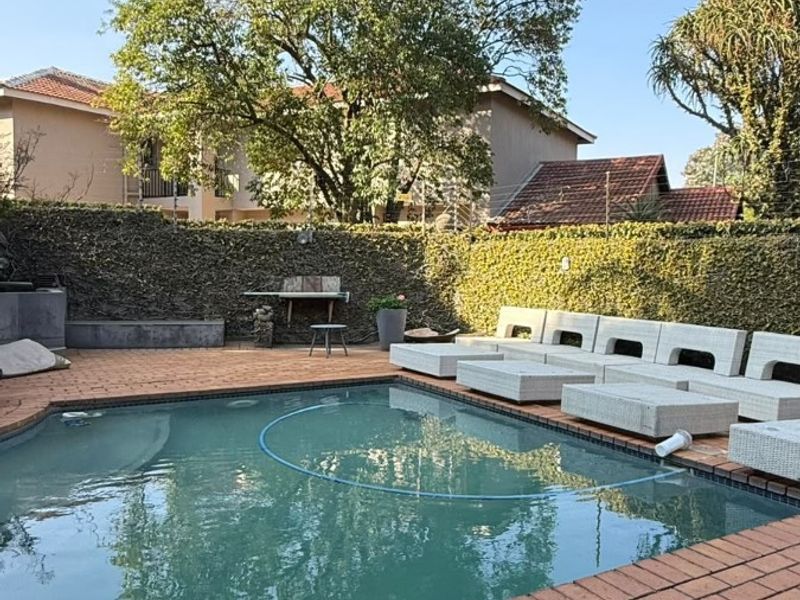 A private outdoor pool area featuring brick paving, a built-in stone bench, and a well-maintained hedge boundary.