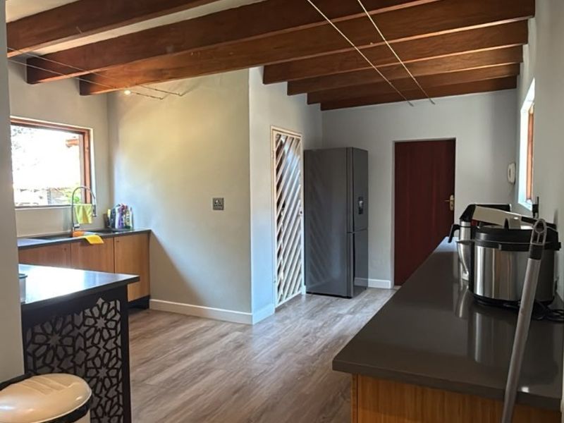 A functional kitchen featuring exposed timber ceiling beams, laminate flooring, and ample stone countertop workspace with integrated cabinetry.