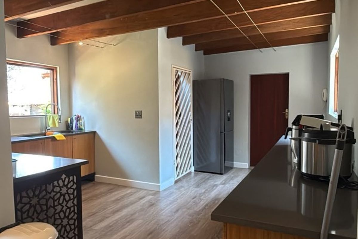A functional kitchen featuring exposed timber ceiling beams, laminate flooring, and ample stone countertop workspace with integrated cabinetry.