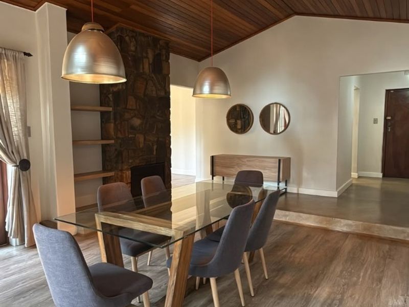 Elegant dining area featuring a striking timber-clad vaulted ceiling, stone fireplace, and warm laminate flooring, creating a sophisticated and inviting atmosphere.