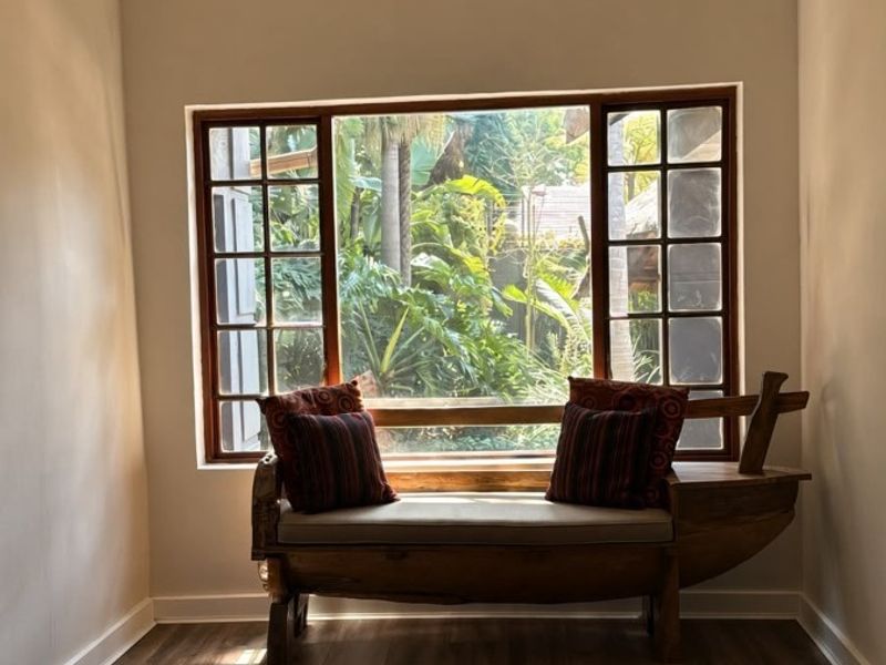 A bright living space featuring timber-look flooring, a large wooden-framed window with garden views, and a modern pendant light fixture.