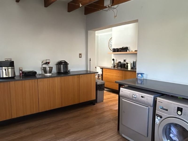 A functional scullery area featuring modern wood-finish cabinetry, stone countertops, durable laminate flooring, and exposed timber ceiling beams.