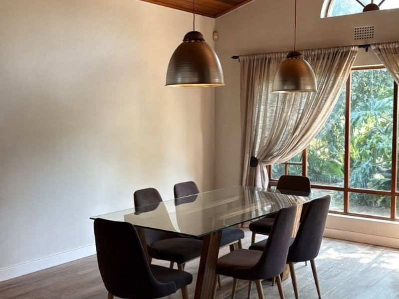 A bright dining room featuring a vaulted timber-clad ceiling, laminate flooring, and an arched window providing natural light.