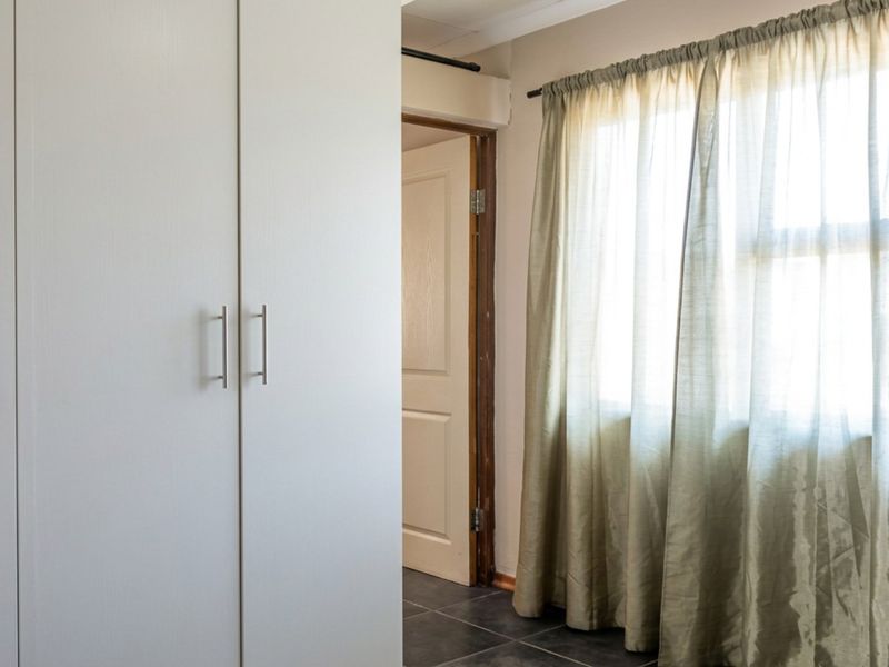 A clean, empty bedroom featuring built-in cupboards, tiled flooring, and natural light through a window.