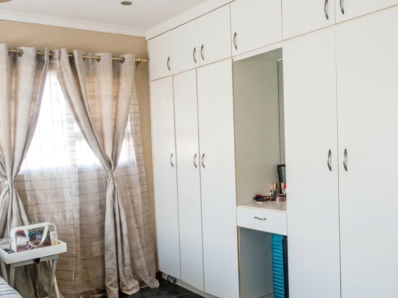 A bedroom featuring extensive white built-in cupboards with an integrated vanity section and recessed ceiling lighting.